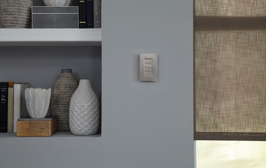 closeup shot of a silver Lutron on-wall keypad in between a shelf and a window
