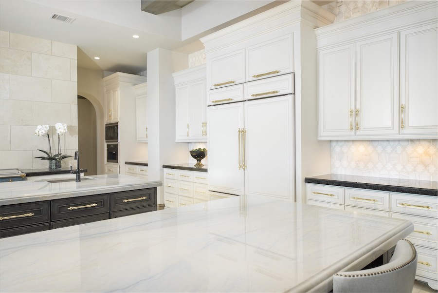 A light, luxury kitchen with modern lighting, cabinetry,  and stone finishes.