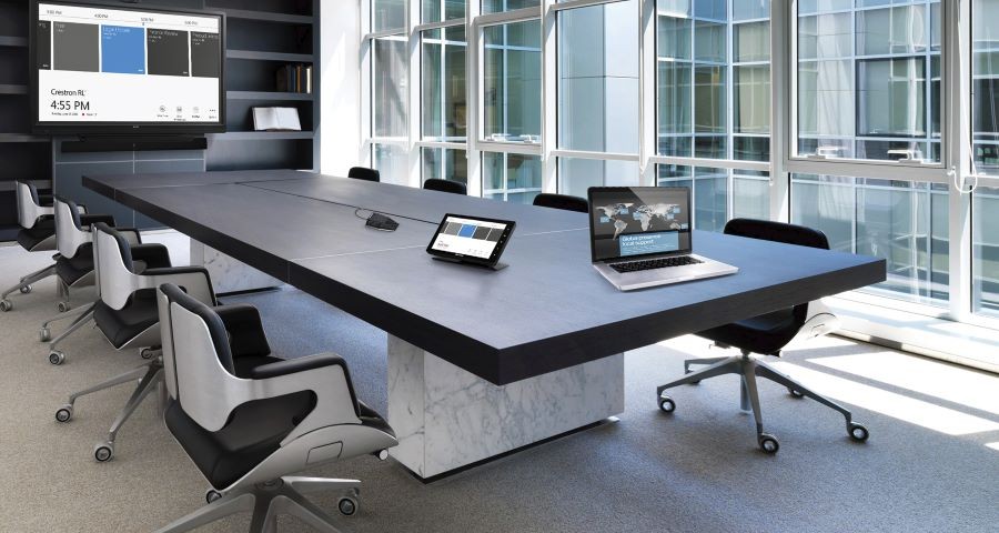 A conference room with a laptop, tablet, and display showing the Crestron interface.
